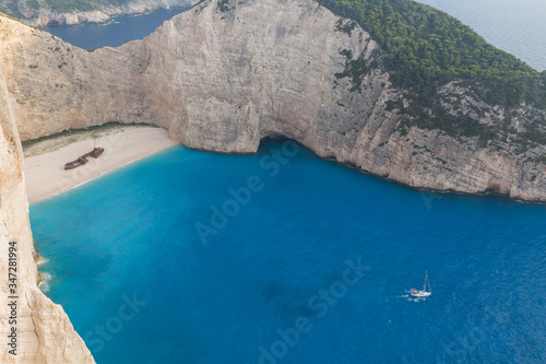 Idyllic view of the beautiful Navagio beach with a sailboat sailing nearby on the island of Zakynthos in Greece.