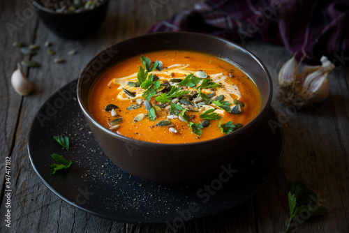 Pumpkin soup with cream, parsley and pumpkin seeds on dark background