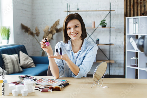 Young female blogger recording a tutorial video for her beauty blog about cosmetics.Vlogger testing nail polish and broadcast live video to social network at home.Blogging, videoblog, makeup concept.