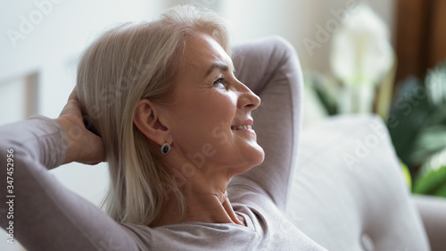 Close up of happy mature woman sit relax on sofa in living room breathing fresh air, smiling calm middle-aged female rest on couch at home daydreaming or enjoying leisure weekend, stress free concept