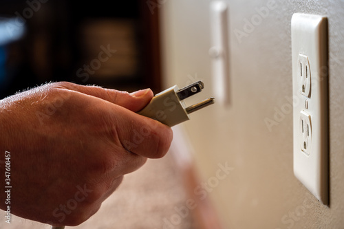 Caucasian hand gripping a three pronged power cord to insertCaucasian hand gripping a three pronged power cord to insert into a power outlet into a power outlet