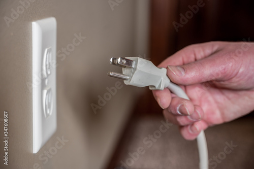 Caucasian hand gripping a three pronged power cord to insert into a power outlet