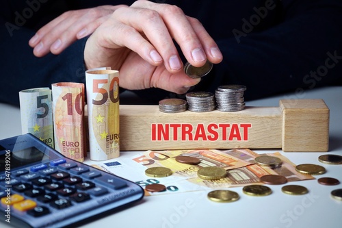 INTRASTAT. Männliche Hand stapelt Geld-Turm (Euro). Begriff an Baustein. Münzen, Scheine & Taschenrechner. Konzept für Business, Finanzen, Statistik