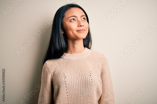 Young beautiful chinese woman wearing casual sweater over isolated white background smiling looking to the side and staring away thinking.