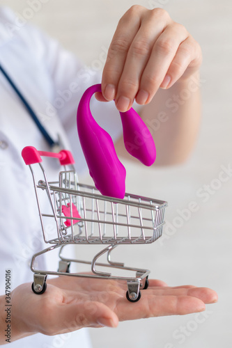 The faceless gynecologist recommends buying a clitoral vaginal vibrator to maintain women's health. The doctor holds a mini trolley and a masturbator for vivid orgasms.