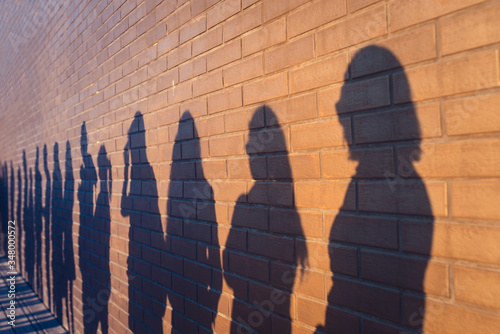 People crowd shadows lined up against a red brick wall. They are in a queue for changes in life. Social distance, covid and immigration issue concept