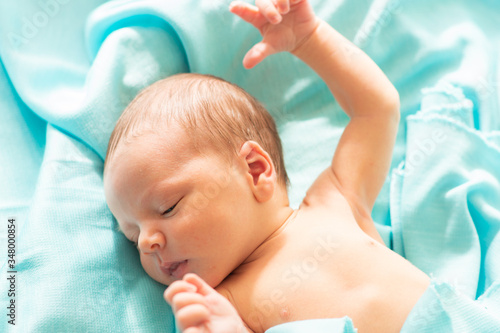 Little caucasian newborn baby falls asleep on blue, delicate and soft blanket. Baby relaxing in safe and calm atmosphere.