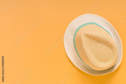 Beige summer straw hat with a blue ribbon on a pastel yellow background. Top view, copy space.