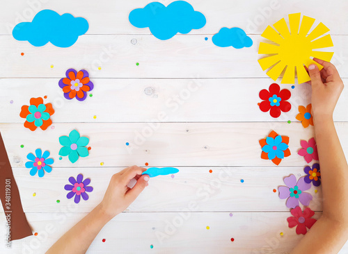 Composition of colorful summer flowers, sun, clouds from multi-colored paper, step by step. Child make crafts his own hands. Cute DIY handmade art creativity on a wooden table. Top view, copy space
