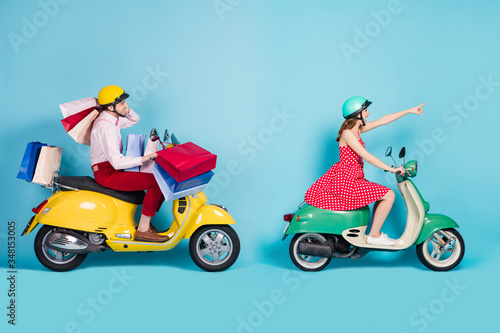 Full size profile photo of crazy shopaholic lady showing next store guy drive retro moped carry packs shopping abroad foreigners vintage clothes protective cap isolated blue color background