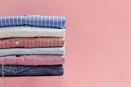 Cropped image with stack of colorful perfectly folded clothing items. Macro shot of pile of different pastel color shirts, sweaters & pants. Close up, copy space, background.