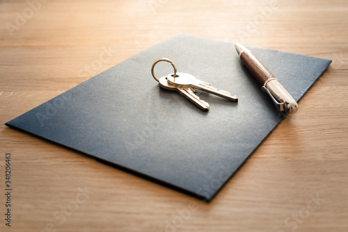 Keys, pen and envelope on the wooden table. Selling or rental of flat, house or another real estate or object. Symbol of agreement