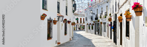 Panoramic image white copy space view, empty street famous village of Mijas in Spain. Charming narrow streets with New Year decorations, hanging flower pots on walls, no people. Costa del Sol, Malaga