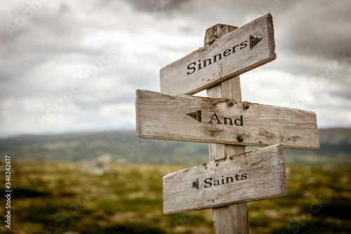 sinners and saints text engraved on old wooden signpost outdoors in nature. Quotes, words and illustration concept.