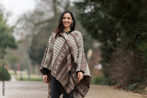 Young Indian woman wearing poncho smiling toothy smile at camera outdoors.