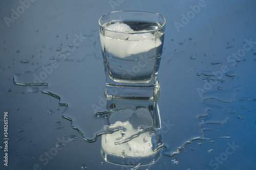 Bartender pouring up frozen vodka from a bottle into two shots glasses with ice cubes against black background. Barman pour of clear transparent alcohol drink rum tequila in shot-glass