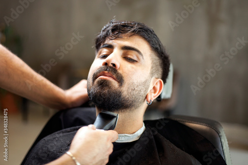 Male hairstylist serving client, making haircut using machine and comb.