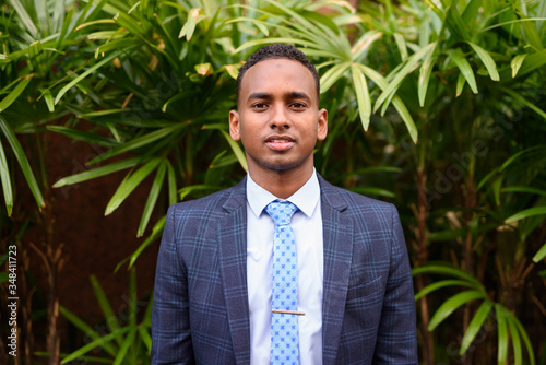 Young handsome African businessman wearing suit in the city with nature outdoors