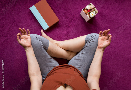 Mujer en cuarentena meditando sobre una manta morada con flores y un libro