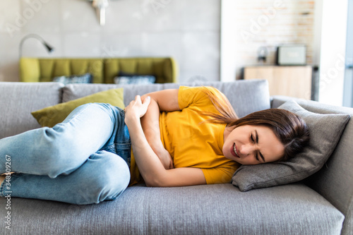 Sick woman lying on sofa in the living room with stomach ache