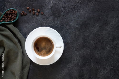 White Cup with fresh coffee on a saucer with coffee beans on a dark background with a green cloth