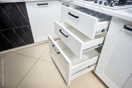 Solution for placing kitchen utensils in modern kitchen - horizontal sliding pullout drawer shelves storage in cupboard for kitchenware cookware under oak countertop gas hob with copyspace.