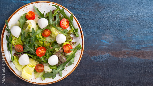 Arugula, lettuce, cherry tomatoes and mozzarella cheese on a plate. Top view, text space