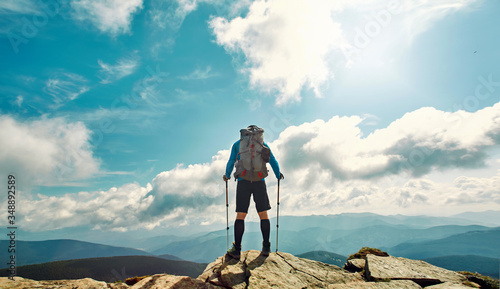 Rear view man traveler hiking stand on top of mountain against beautiful cloudy sky, enjoying nature view, solo traveling. Outdoor adventure, wild journey, people in nature