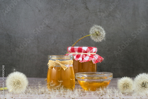 Dandelion jam, honey, jelly in a glass jar on a wooden table, black background with fresh flowers, dandelion airy seed heads, seeds, blow balls. Medicine, healthy food, health benefits from nature