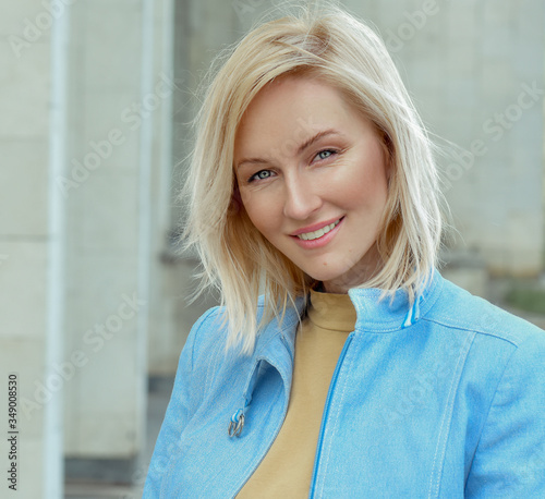 Young attractive woman in a bright blue denim and jeans jacket. Business woman looks at the camera. wind in the hair blonde with blue eyes. walk on a sunny day. sexy girl walks on the street