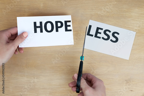 Woman hands cut the word hopeless, in one hand holds word "hope", the prefix "less" lies on the table