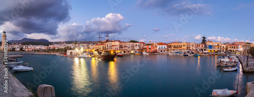 Venetian Harbour panorama with boats in front of restaurants at sunrise under colored clouds. Rethymno, Crete, Greece