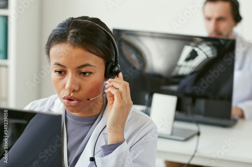 Young woman wearing headphones working on computer she answering on phone calls in medical call centre