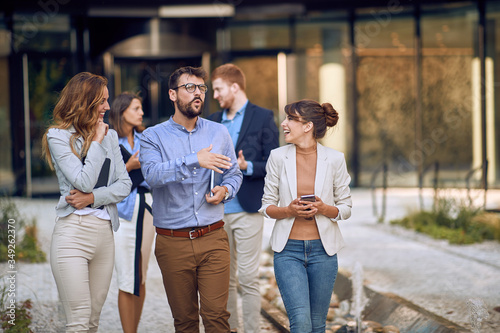 young business people in front of a building, carrying tablets, cell phones, folders. witty colleague telling funny story. female colleagues laughing