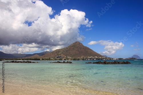 Stunning panoramic view to scenic lagoon with shallow water sand beach and black stones surrounded mountains and fantastic blue sky with low fluffy white clouds on background.Winter season Mauritius