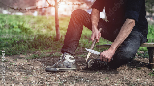 Man sharpening a stake outdoors. Male using a hunting knife and cutting a small branch. Bushcraft, camping and survival concept.
