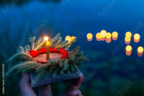 A hand holds a wreath and a fire on a Board close-up, a mysterious ancient Slavic pagan ritual, the light of lights on the lake in a blurred background