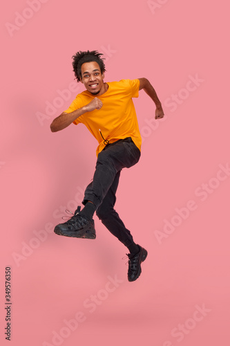 Bottom view full length shot of funny young male african american guy dancing and jumping on pink background in studio. Concept of good news and special offers for millennials. Advertising space