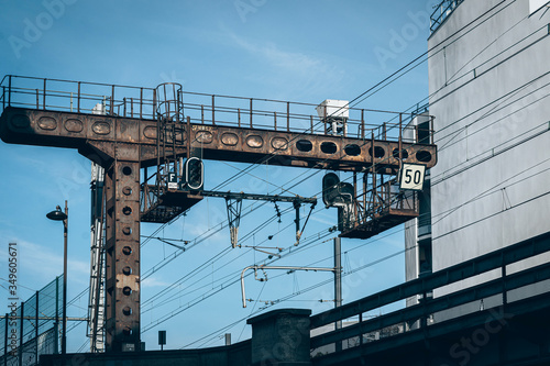 Train tracks that pass near the houses of the city, it is a noisy area, there is a rusty metal bridge and cables and catenary