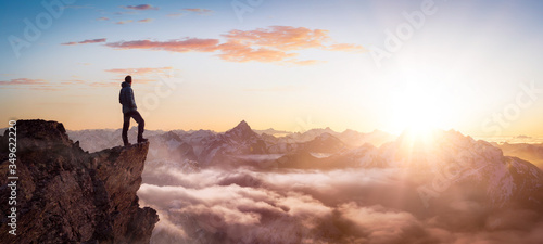 Magical Fantasy Adventure Composite of Man Hiking on top of a rocky mountain peak. Background Landscape from British Columbia, Canada. Sunset or Sunrise Colorful Sky