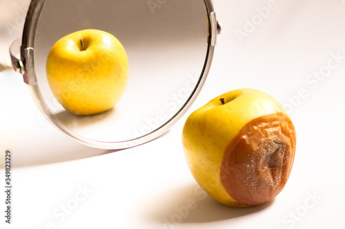 Apple in good condition looking at itself in the mirror while its back is rotten. Psychological concept, deception