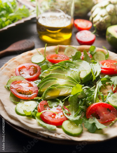 Cooking Delicious tortilla with cherry tomatoes, avocado, cucumber, arugula and olive oil. On a rustic wooden table, with ingredients laid out around. The idea of ​​a healthy dish. Close up.