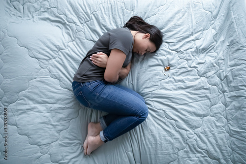 Deeply unhappy depressed african mixed race young woman lying on bed near bottle and heap of pills, above view. Medication abortion, suicide, taking somnifacient anti depressant overdose drug concept