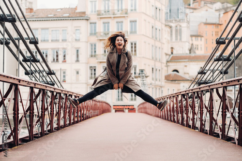 a girl in a coat with her hair down jumps emotionally on a bridge in the old city of Lyon. France. Girl in a coat in France