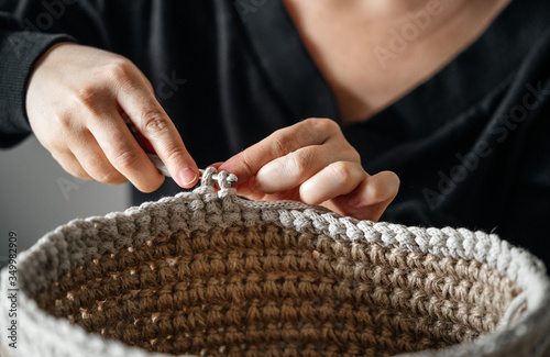 Handwork and hobbies. Female hands crochet a basket for the interior from a jute thread.