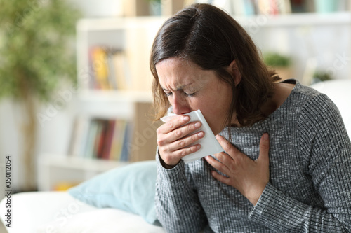 Sick adult woman coughing covering mouth with tissue at home