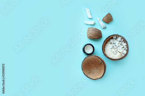 Coconut cut into pieces, coconut shavings, green leaves, shea butter on a blue background. A place for text.