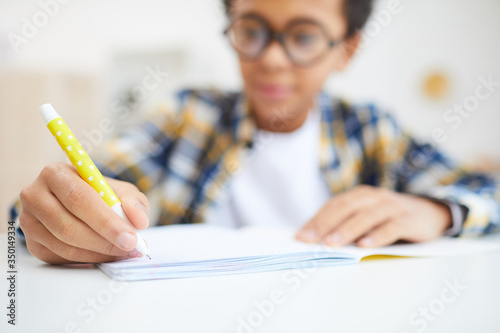 Close up of cute African boy writing in notebook while doing homework, focus on foreground, copy space