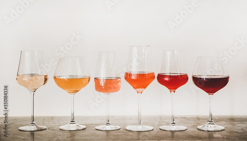 Various shades of Rose wine in stemmed glasses placed in line from light to dark colour on concrete table, white wall background behind. Wine bar, wine shop, wine tasting concept