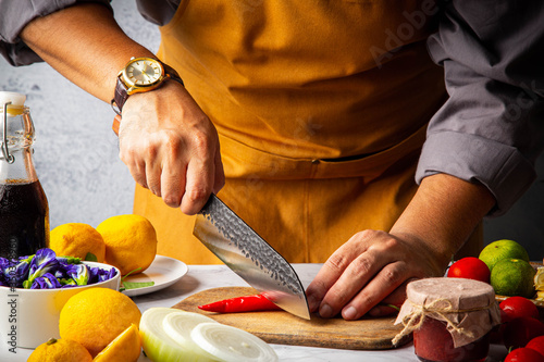 Male slicing chilli pepper on wooden cutting board by Japanese kitchen damaskus knife (Santoku) to preparation for meal in home kitchen